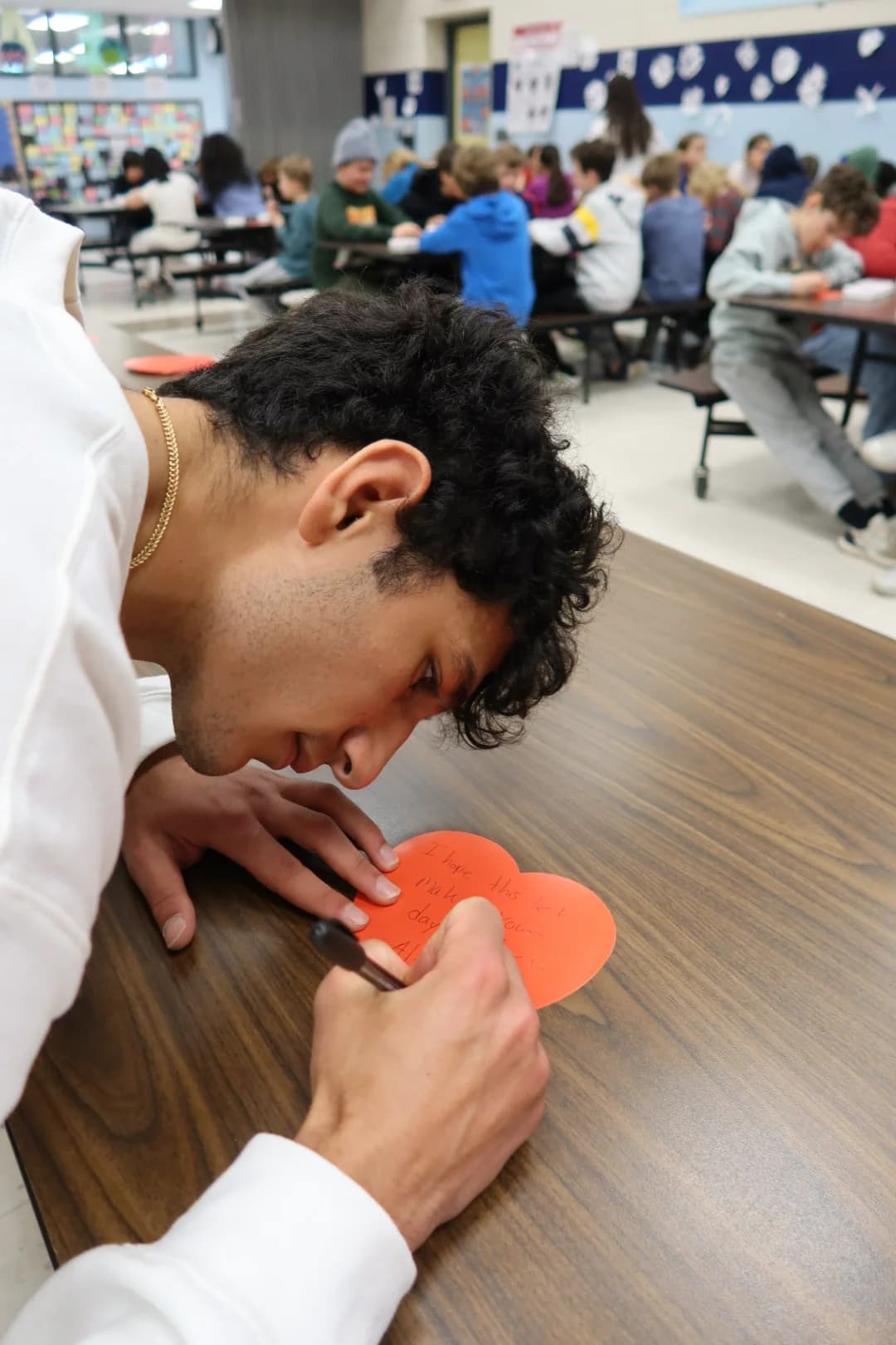 A student writing a personalized heart-shaped note for a care kit recipient