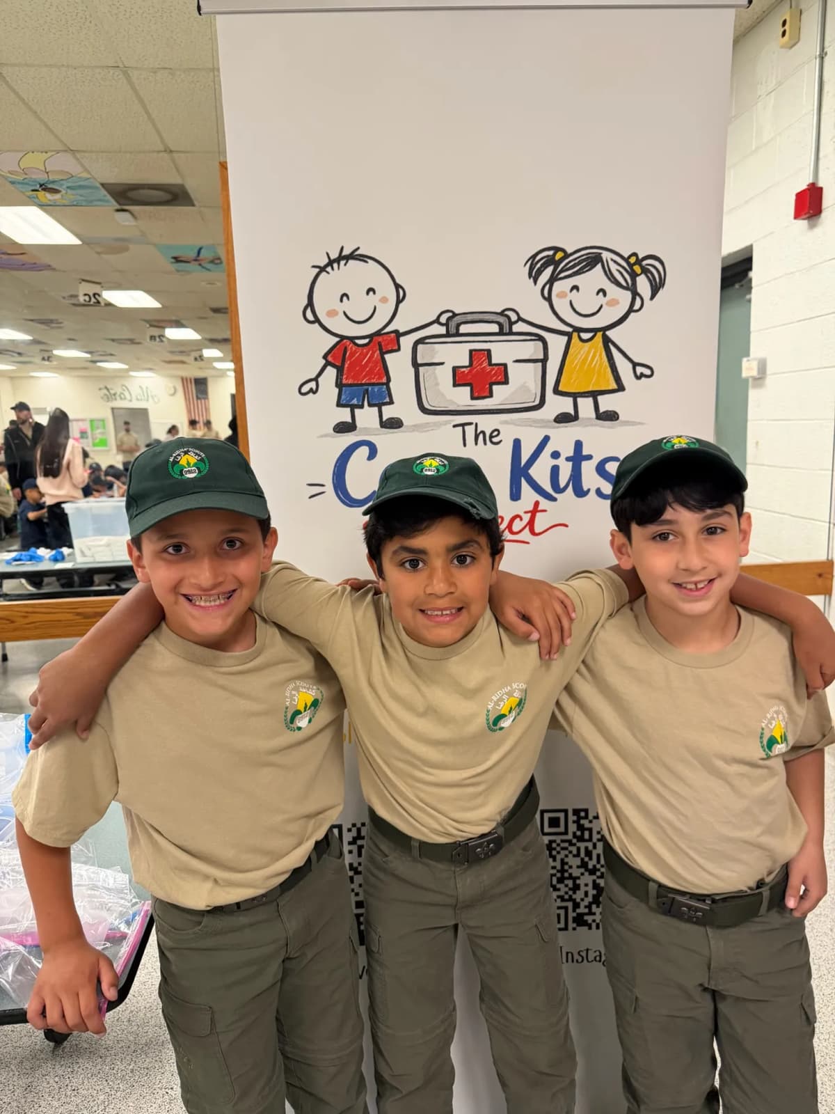 Three young scouts smiling in front of the Care Kits Project banner